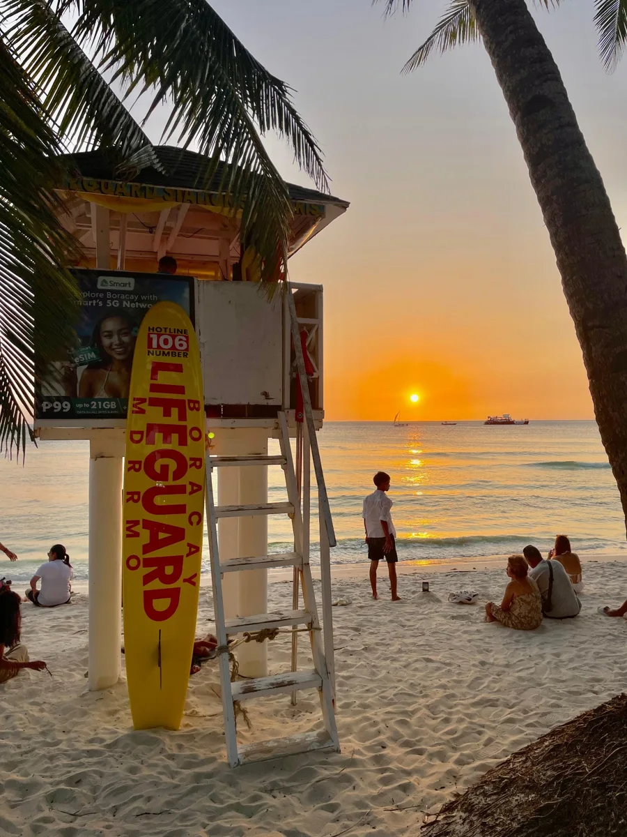 Lifeguard tower and beachgoers beneath palms at sunset in Boracay