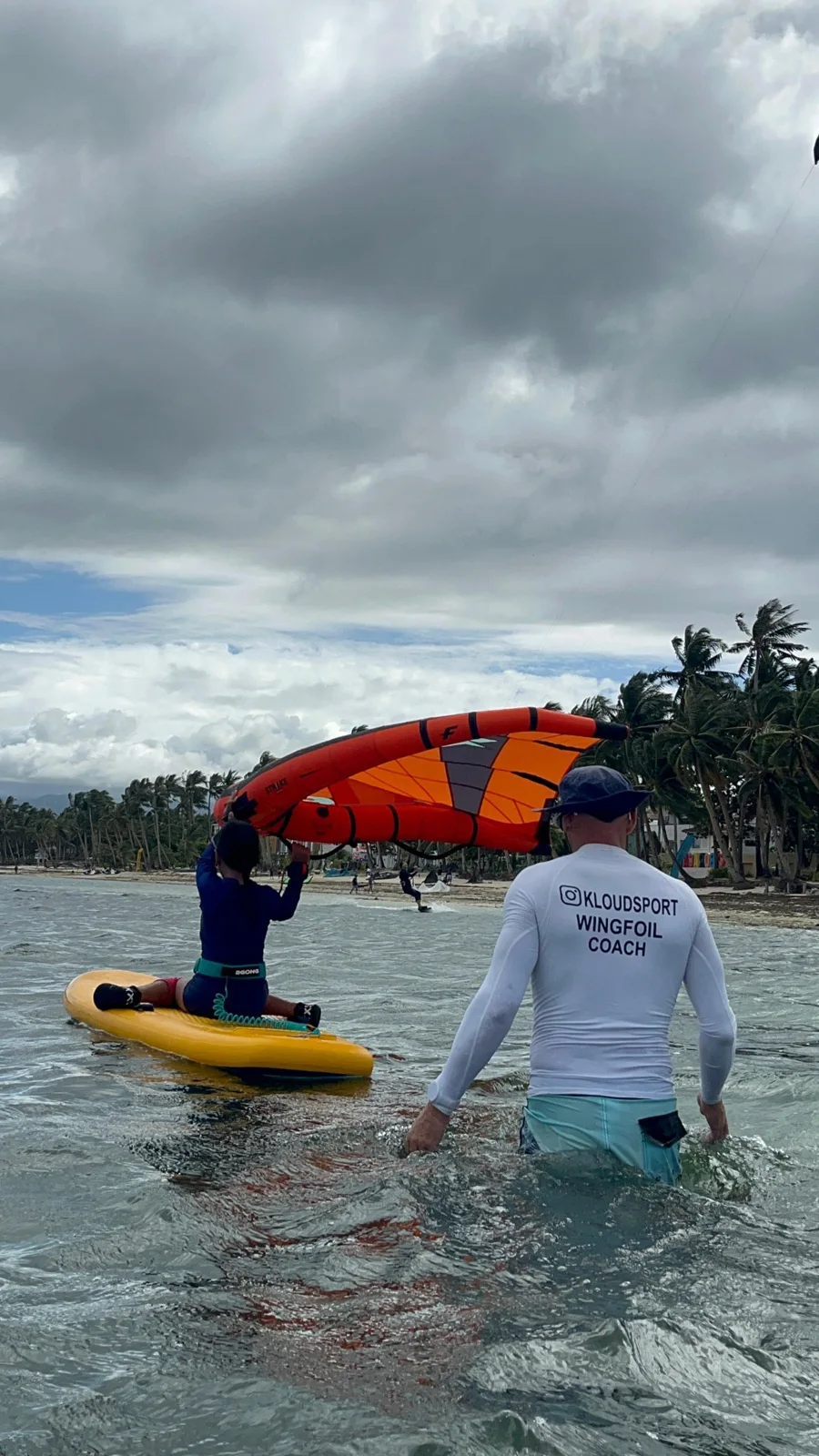 An instructor accompanying a learner with an orange wing and a yellow board