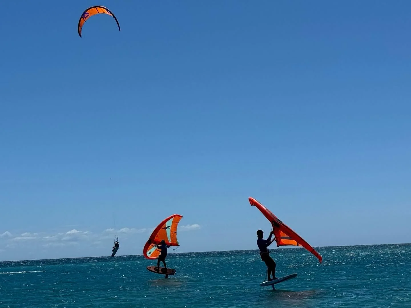 Two wing foilers riding offshore with kites in the background