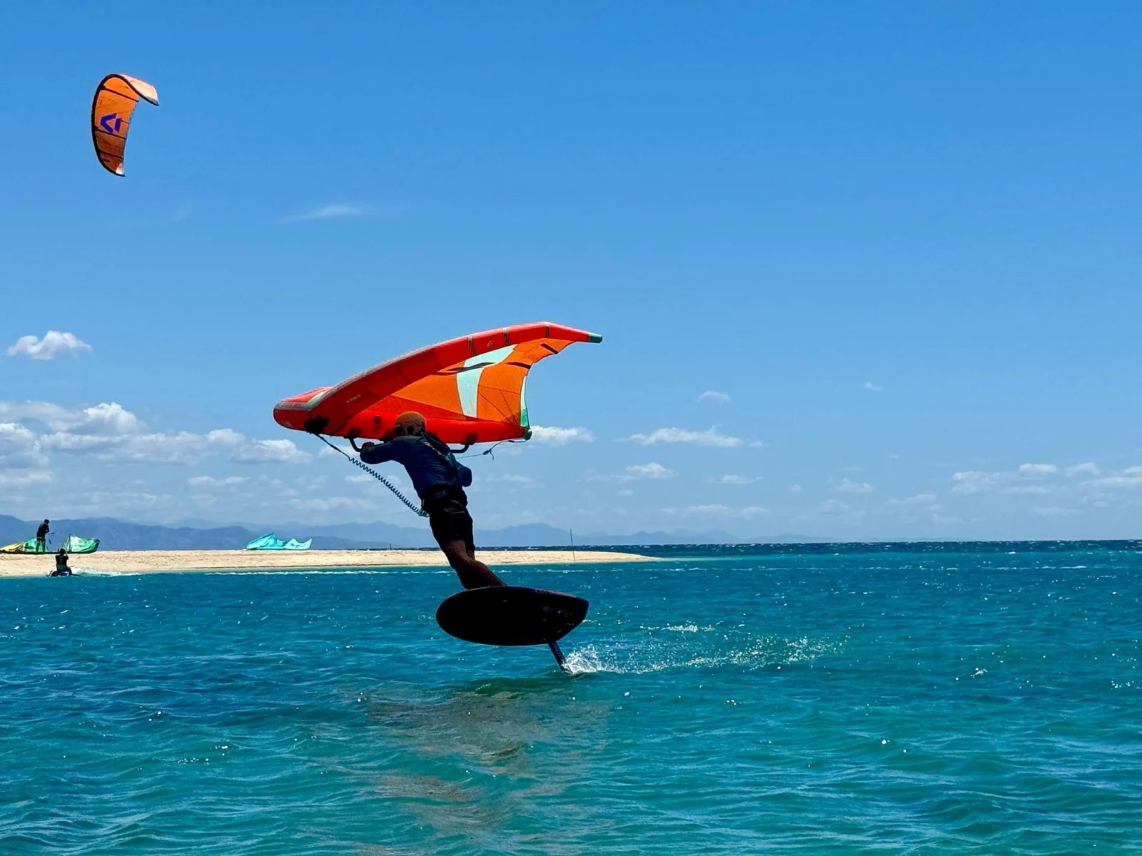 A wing foiler riding an orange wing on turquoise water off Boracay