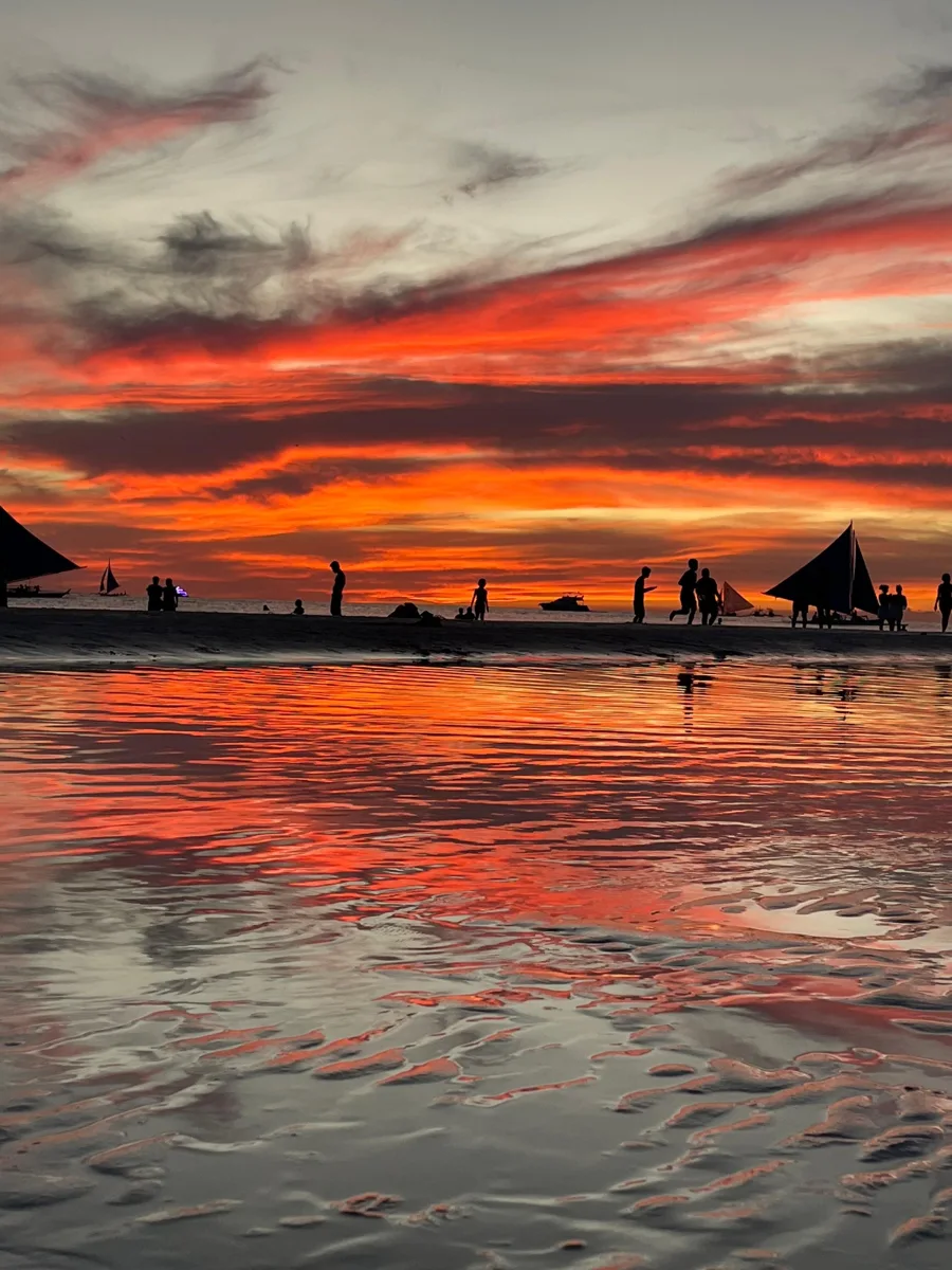 Sailboats silhouetted against a red and orange sunset over Boracay