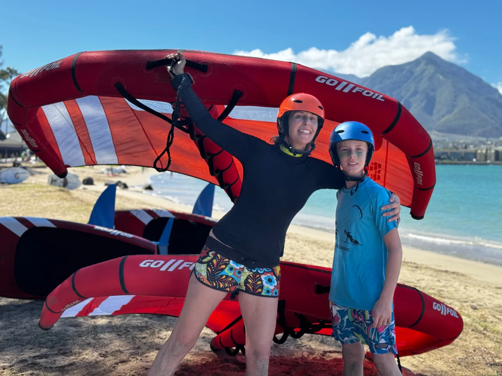 Two riders posing beside wing-foil equipment
