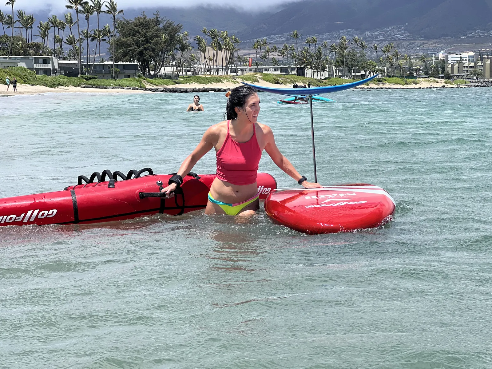 Rider beside a red board and wing in shallow water