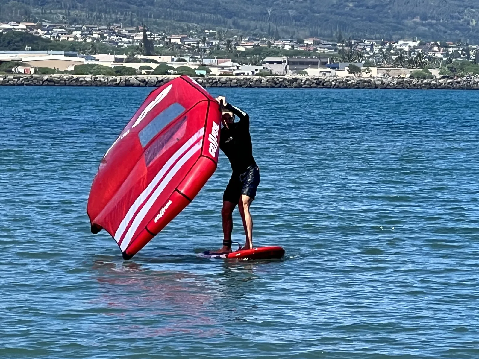 Wing foiler riding a board with a red wing on the water in Maui