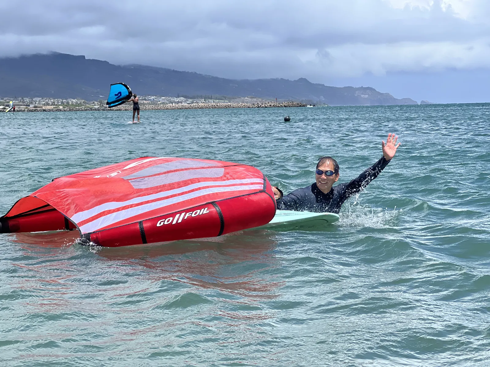 Rider waving beside a red wing during a Maui water session